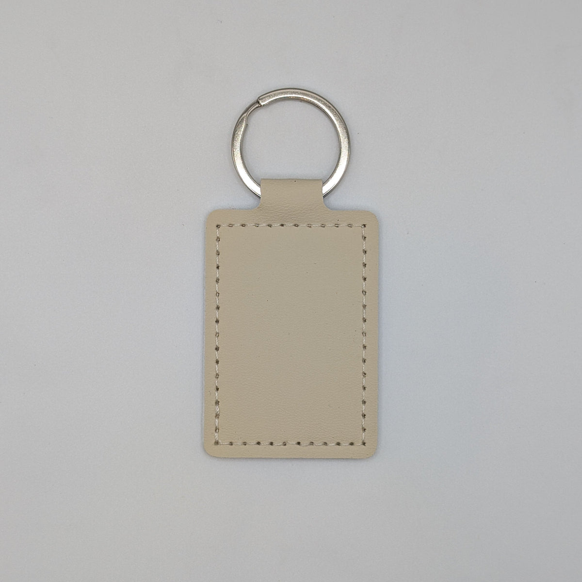 A minimalist beige leather keychain tag with a silver split ring, shown against a neutral light gray background.