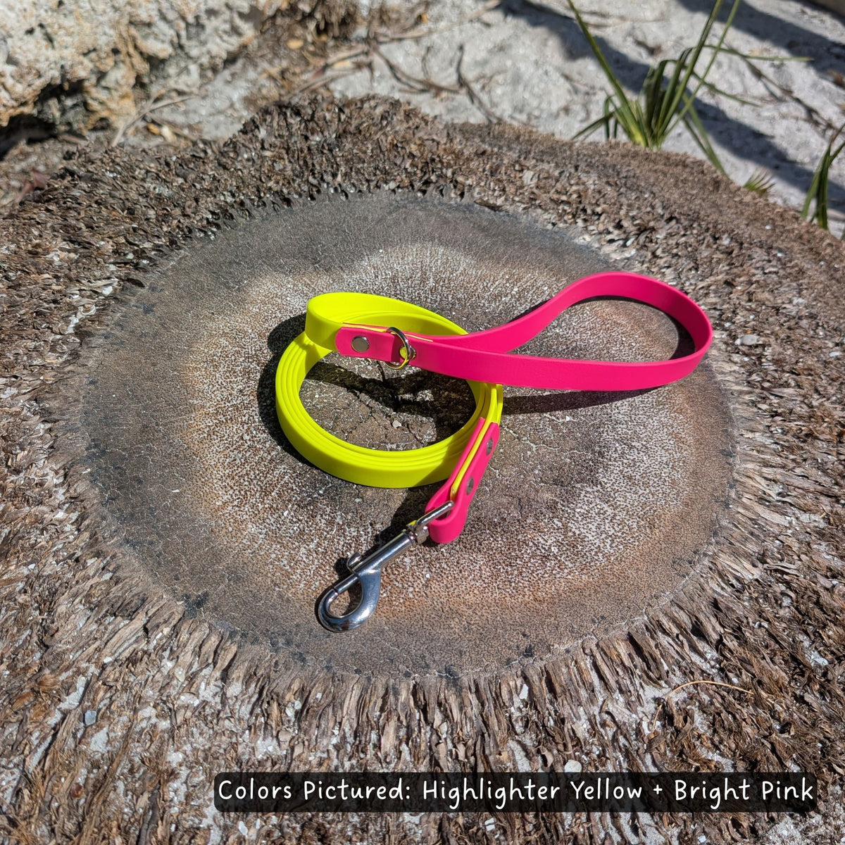 Highlighter yellow and bright pink dog leash made with BioThane and a heavy duty clip. They are laid out on a palm tree stump, with text indicating the colors.