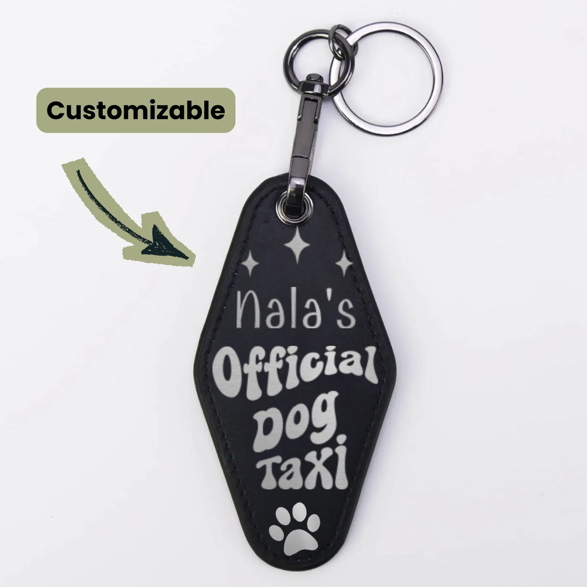 A black custom pet keychain shaped like a coffin, featuring the text 'Nala's Official Dog Taxi' in white lettering with a paw print at the bottom. It is shown with a silver split ring and clasp on a white background, with a 'Customizable' label and arrow graphic on the left.