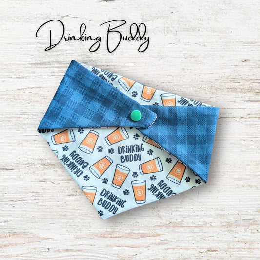 Dog bandana with 'Drinking Buddy' text and beer graphic on a wooden surface, branded 'Drinking Buddy'.
