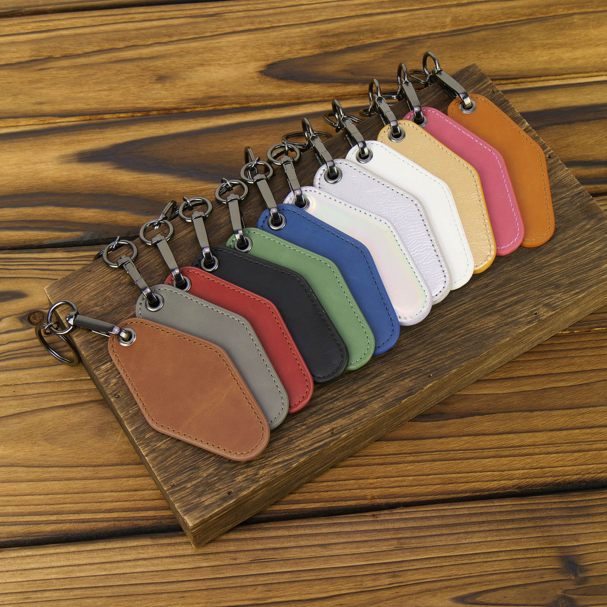 A set of twelve leather keychain tags in various colors, arranged in a fan shape on a rustic wooden board over a wooden table.