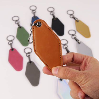 Hand holding a brown leather keychain with colorful tags in the background