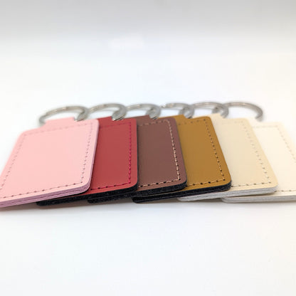 Six rectangular leather keychain tags in pink, red, brown, tan, white, and beige, arranged in a row with silver metal key rings on a white background.