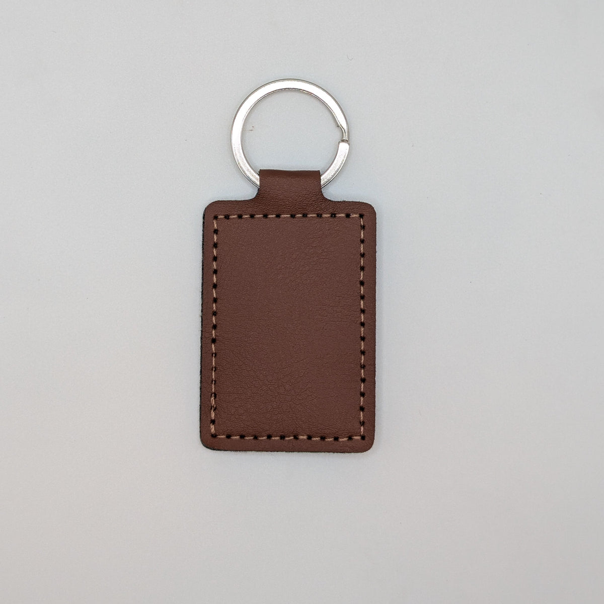 A brown leather rectangular keychain tag with a silver metal split key ring, shown against a plain light gray background.
