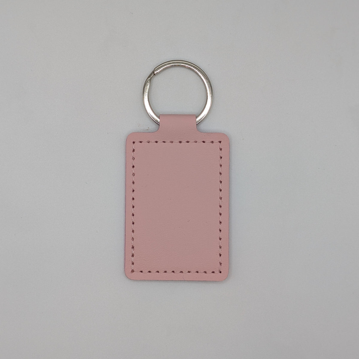 A rectangular pink leather keychain tag with stitched borders and a silver metal key ring, centered on a light gray background.