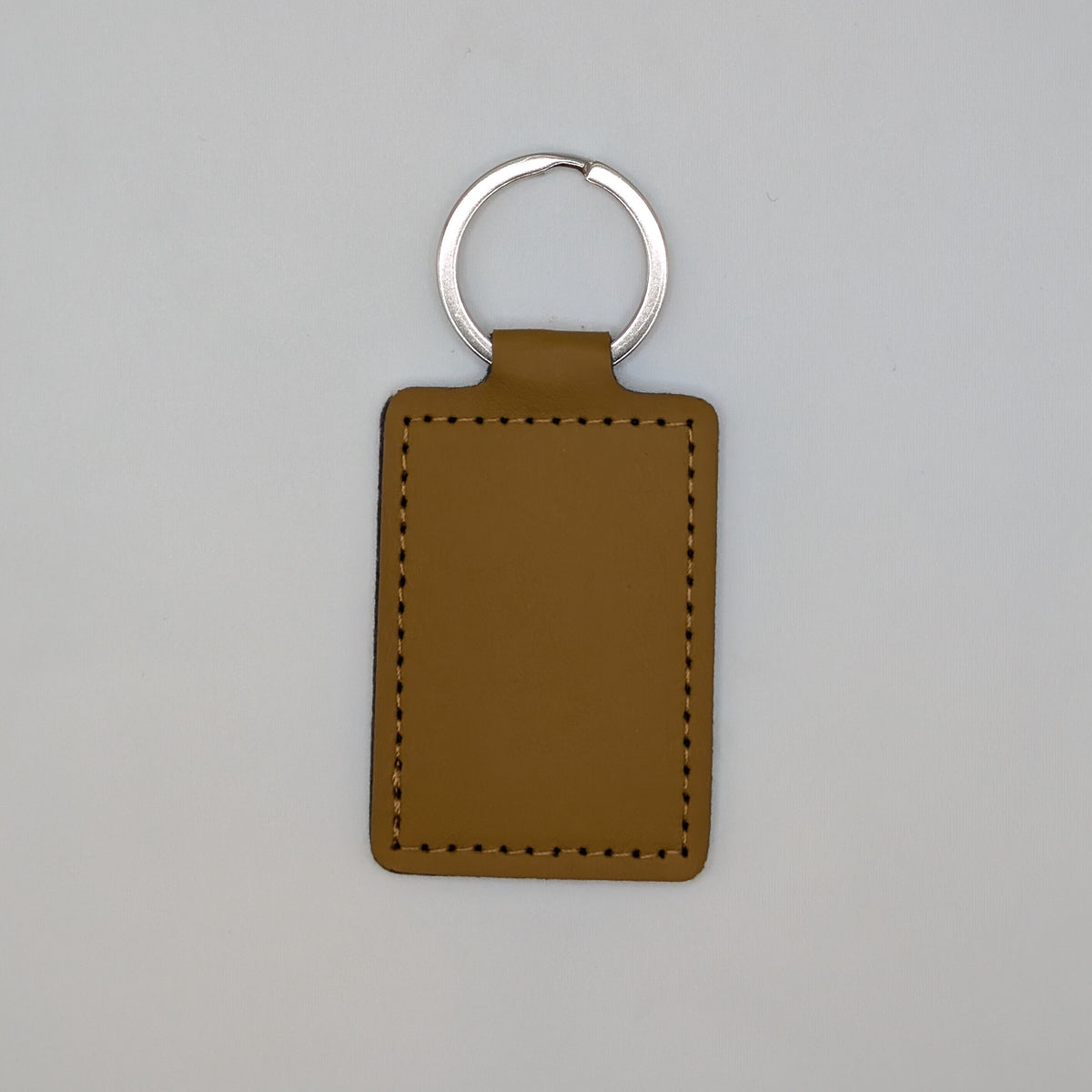 A rectangular brown leather keychain tag with stitched borders and a silver metal key ring, centered on a light gray background.