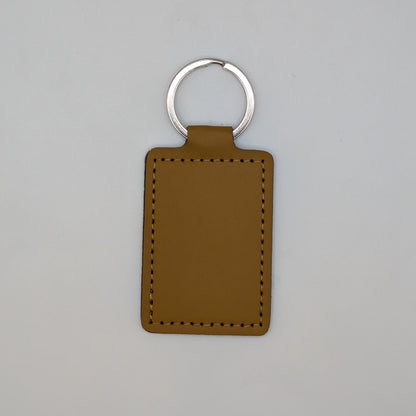 A rectangular brown leather keychain tag with stitched borders and a silver metal key ring, centered on a light gray background.
