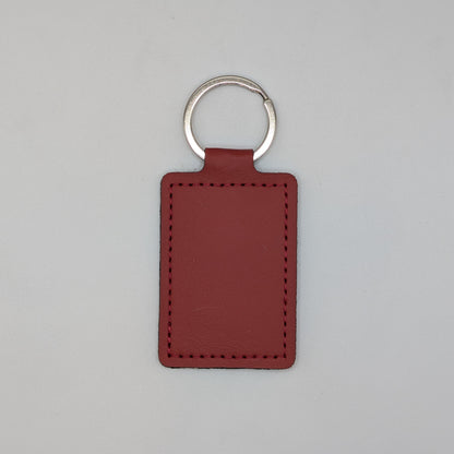 A rectangular leather keychain tag in a reddish-brown color with a silver metal split ring, shown against a plain light gray background.