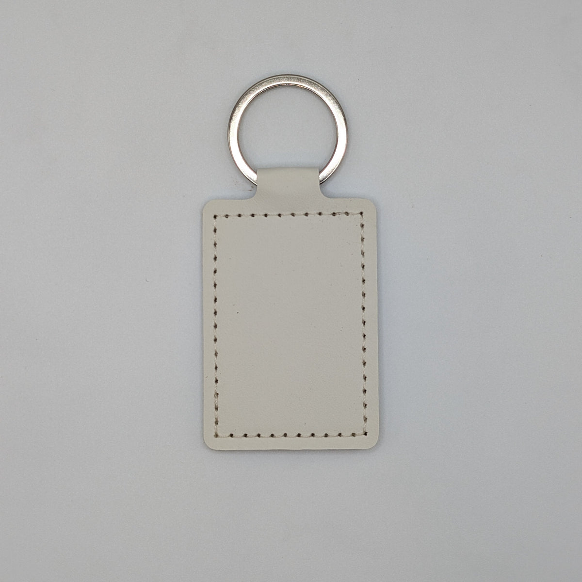 A blank rectangular leather keychain tag with a silver metal split ring, shown on a neutral light gray background.