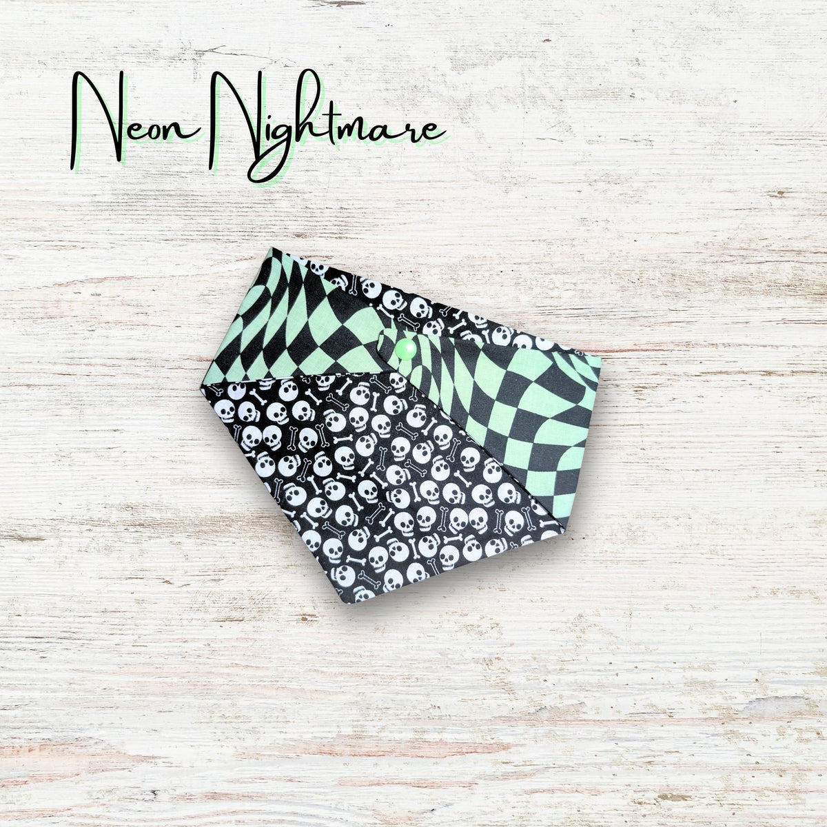 Two patterned pet bandanas on a light wooden surface with 'Neon Nightmare' text. The bandana has skulls and bones on one side with a trippy green checkered print on the reverse side