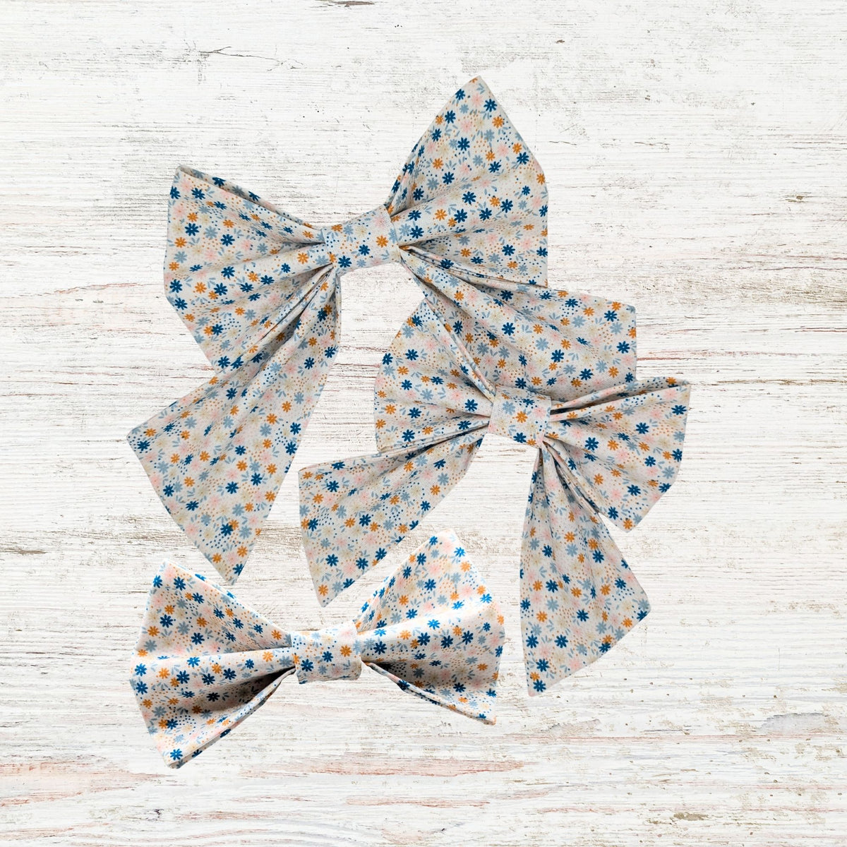 Three floral-patterned pet bows on a light wooden surface