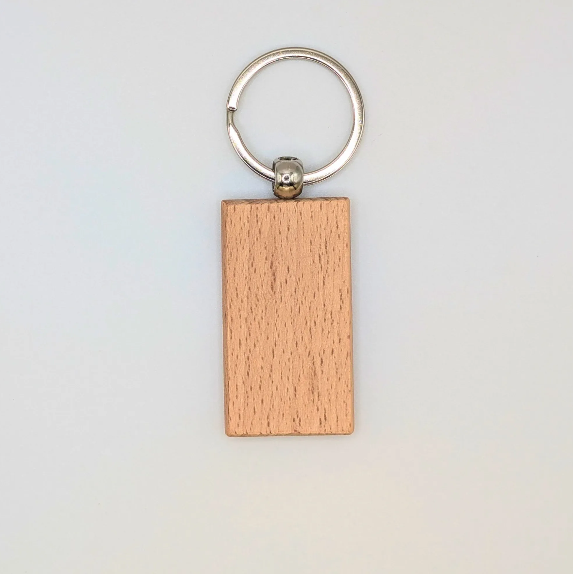 A rectangular wooden keychain with a natural light brown wood grain finish, attached to a silver metal split keyring, shown against a plain off-white background.