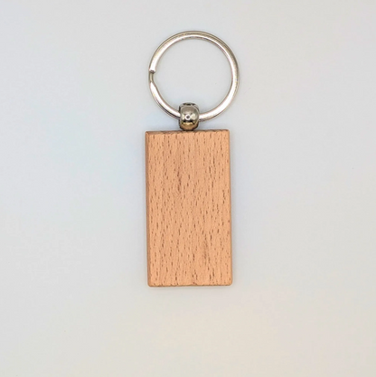 A rectangular wooden keychain with a natural light brown wood grain finish, attached to a silver metal split keyring, shown against a plain off-white background.