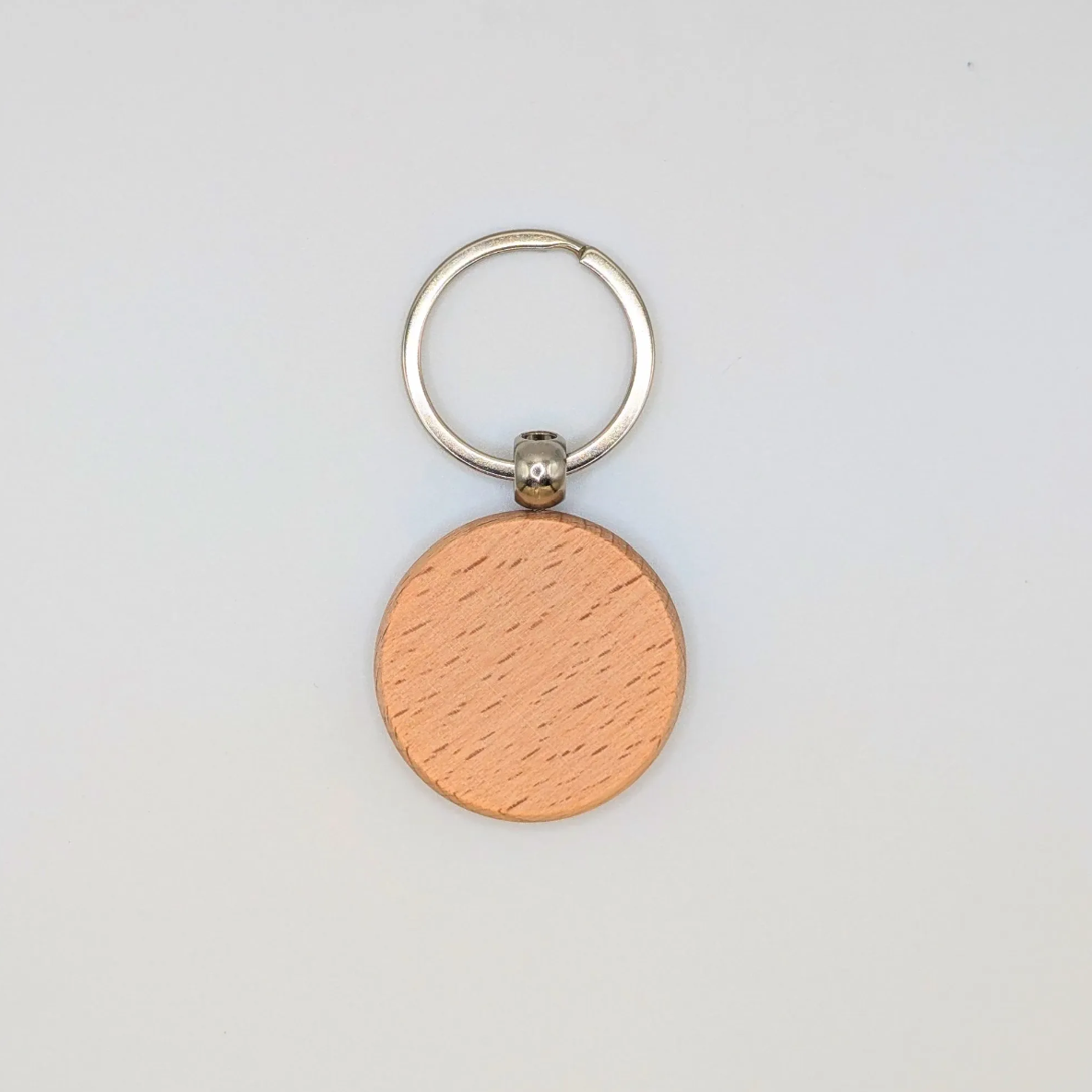 A minimalist round wooden keychain with a natural wood grain finish and a silver split ring, shown on a clean white background.