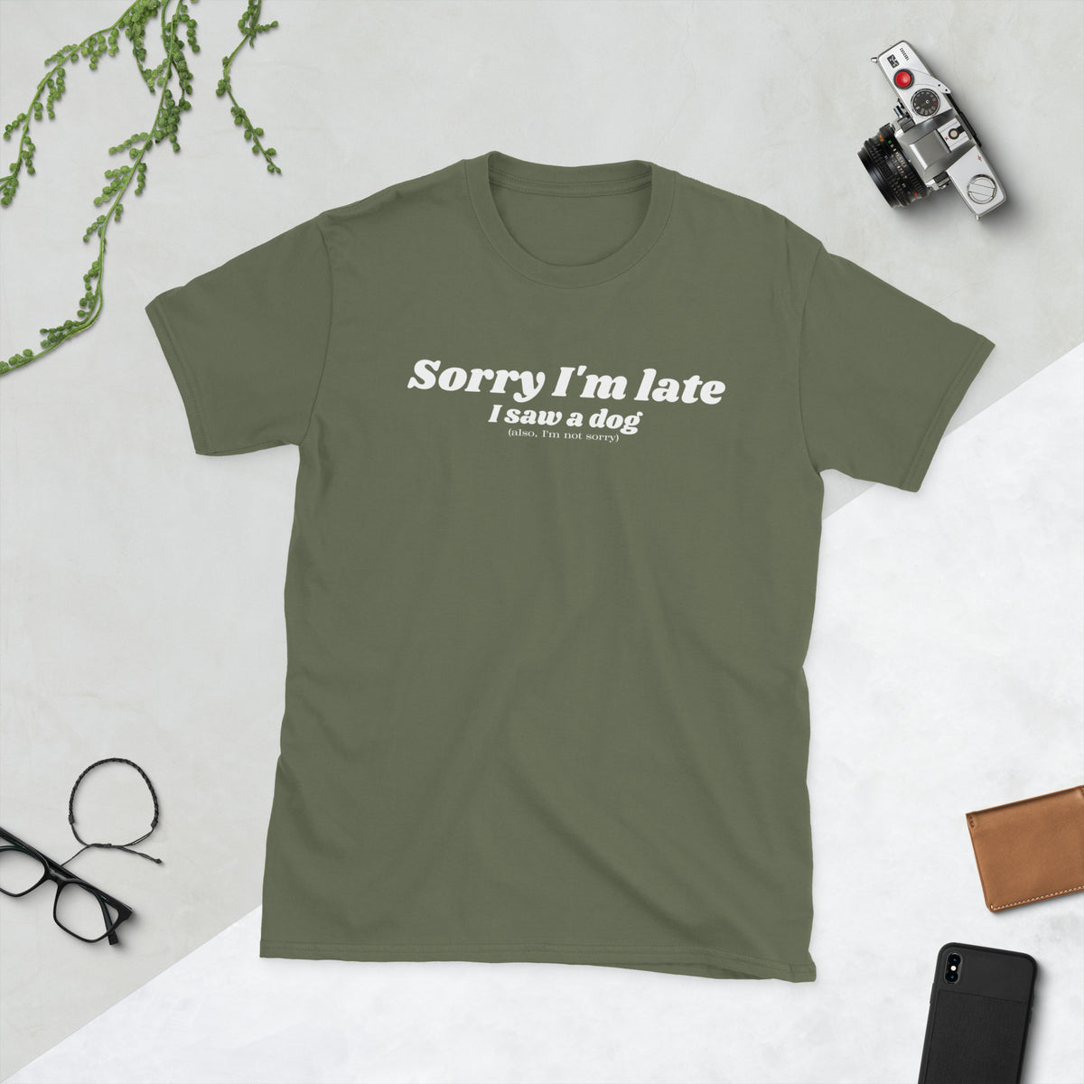 Product mockup of a t-shirt that says 'sorry I'm late I saw a dog. also I'm not sorry'. the shirt is olive green